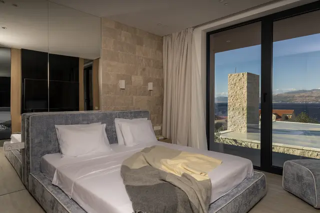 Bedroom in travertine and oak, pool and sea through the glass